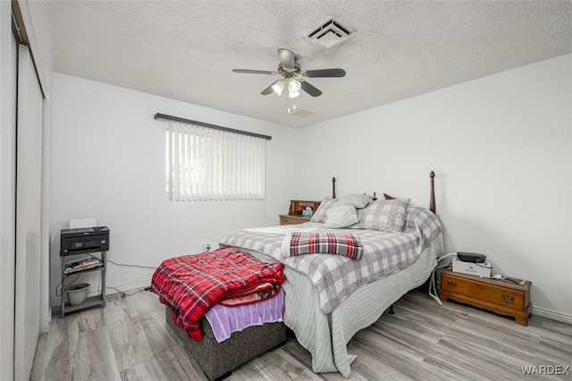 bedroom featuring light wood finished floors, a ceiling fan, visible vents, and a textured ceiling