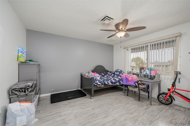 bedroom with light wood finished floors, baseboards, visible vents, and a textured ceiling