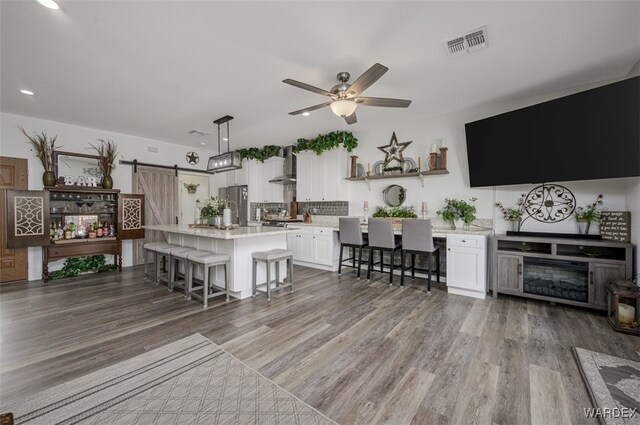 kitchen with a center island with sink, visible vents, a breakfast bar area, freestanding refrigerator, and white cabinetry