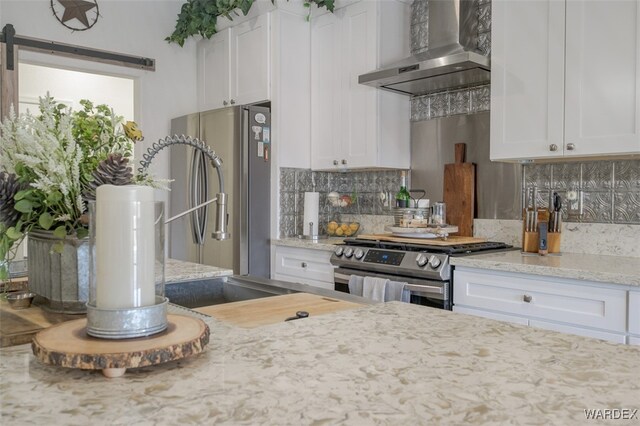 kitchen with appliances with stainless steel finishes, backsplash, white cabinetry, and wall chimney range hood