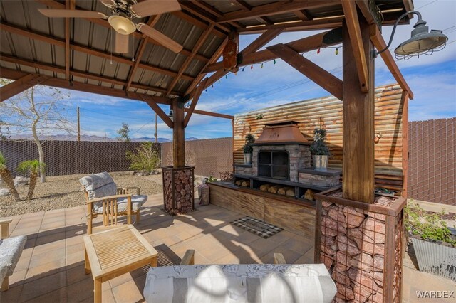 view of patio featuring ceiling fan, a gazebo, an outdoor stone fireplace, and a fenced backyard