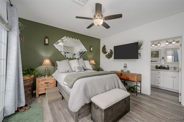 bedroom with light wood-type flooring, visible vents, ceiling fan, and ensuite bath