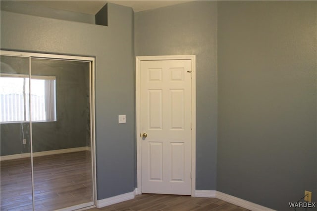 unfurnished bedroom featuring wood finish floors, a closet, and baseboards