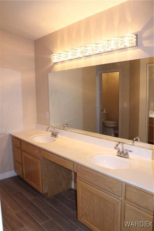 full bath with toilet, double vanity, a sink, and wood finish floors