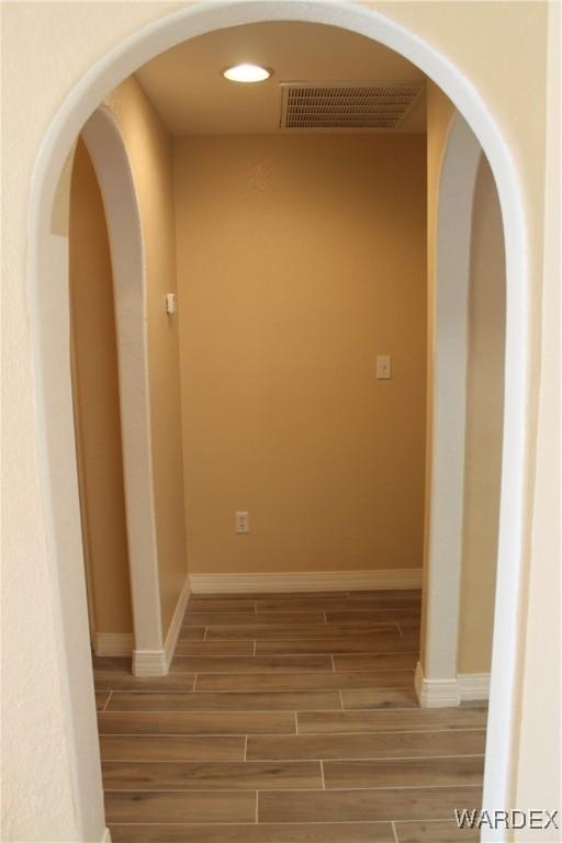 corridor featuring baseboards, visible vents, arched walkways, wood finish floors, and recessed lighting