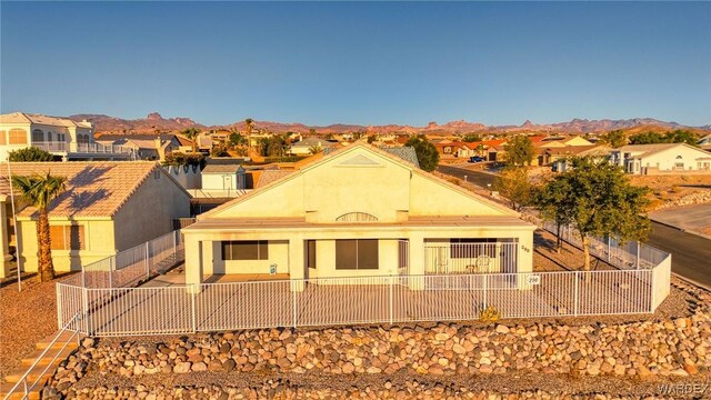 back of house featuring a fenced front yard, a residential view, a mountain view, and stucco siding