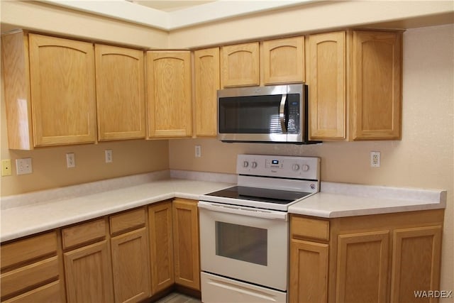 kitchen featuring light countertops, light brown cabinetry, stainless steel microwave, and white range with electric stovetop