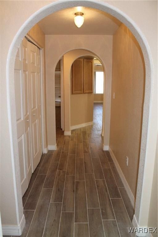 hallway featuring wood tiled floor, arched walkways, and baseboards