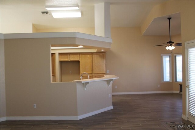 kitchen featuring dark wood-style floors, a breakfast bar, light countertops, a ceiling fan, and baseboards