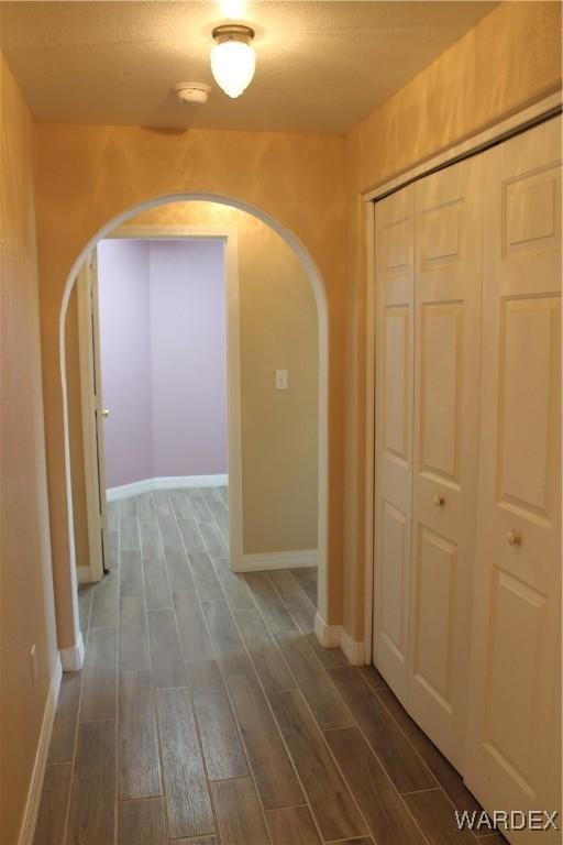 corridor featuring dark wood-style floors, arched walkways, and baseboards