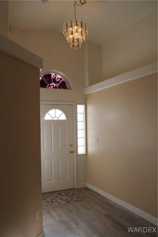 entryway with baseboards, wood finished floors, lofted ceiling, and an inviting chandelier