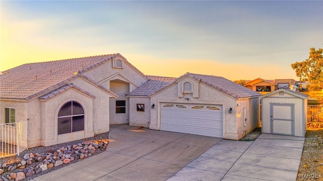 mediterranean / spanish house with a tile roof, driveway, a storage shed, and stucco siding