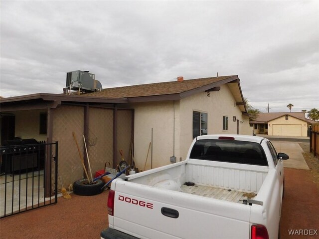 view of side of home with a shingled roof, central AC, and stucco siding