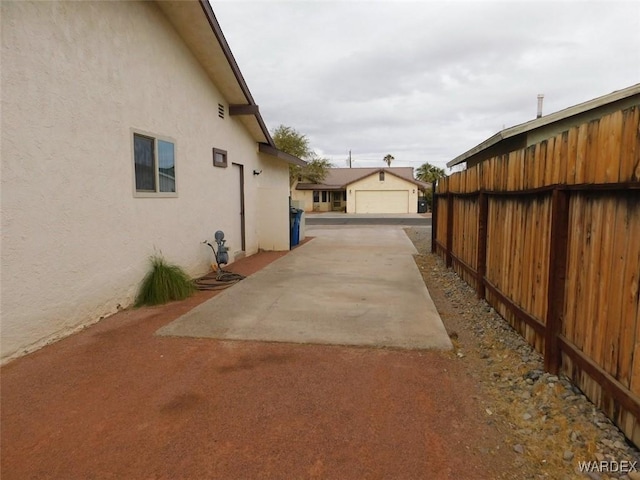 view of side of property with a garage, an outdoor structure, fence, and stucco siding