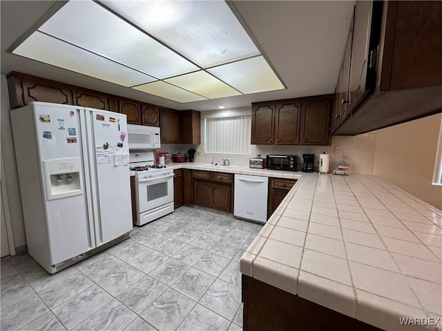 kitchen with white appliances, a toaster, tile countertops, dark brown cabinets, and a sink