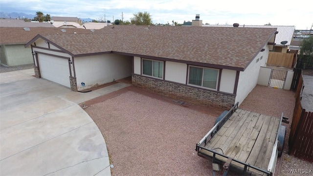 tudor-style house featuring concrete driveway, roof with shingles, a gate, and stucco siding