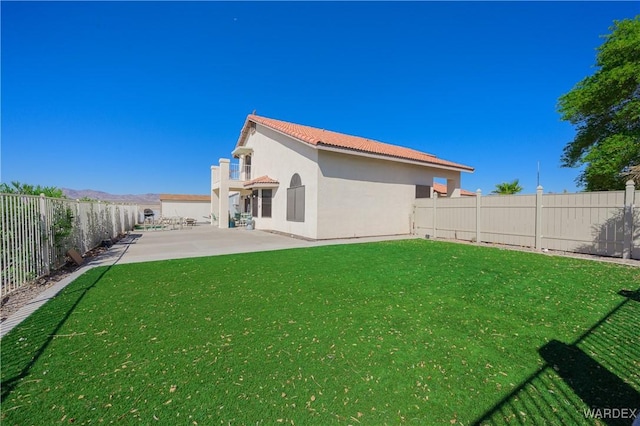 rear view of property with a patio, a fenced backyard, a tiled roof, a yard, and stucco siding