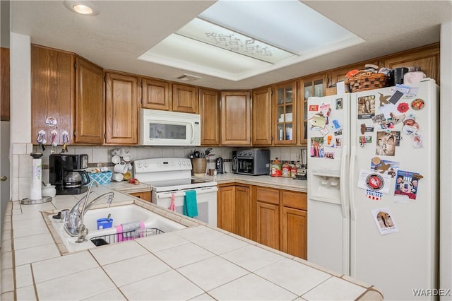 kitchen with glass insert cabinets, white appliances, visible vents, and brown cabinets