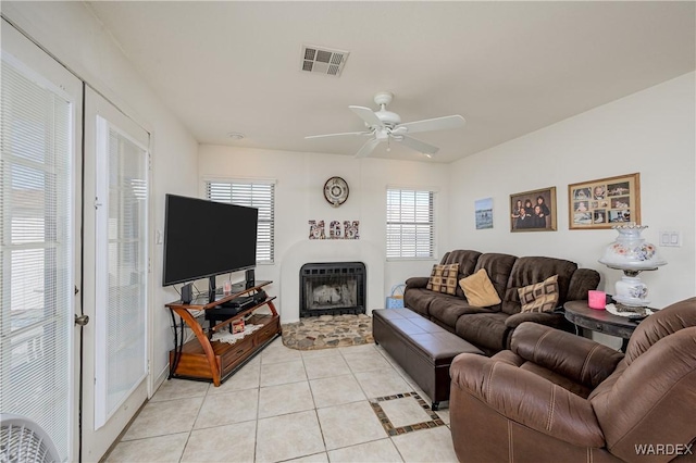 living area with light tile patterned floors, a fireplace with raised hearth, visible vents, and a ceiling fan