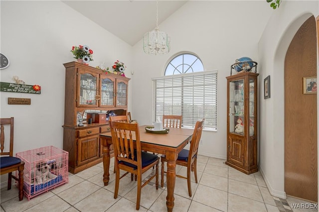 dining space with light tile patterned floors, baseboards, arched walkways, high vaulted ceiling, and a chandelier