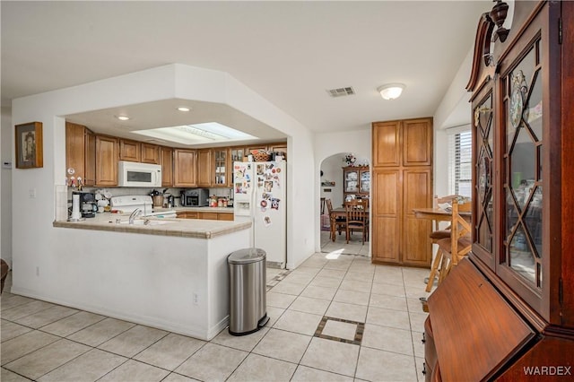 kitchen with brown cabinets, white appliances, light countertops, and a peninsula