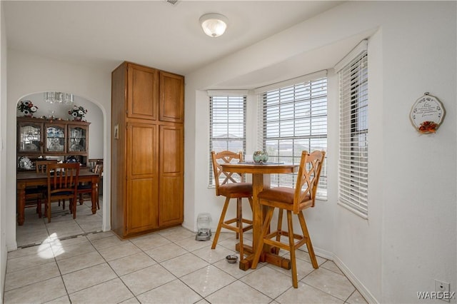 dining space featuring arched walkways, light tile patterned floors, and baseboards