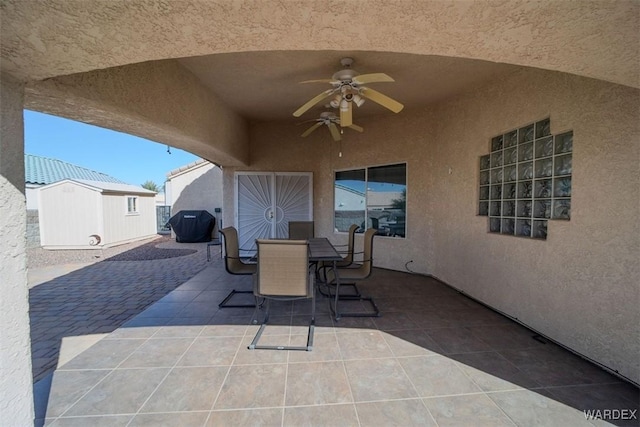 view of patio with an outbuilding, outdoor dining space, a storage unit, and a ceiling fan