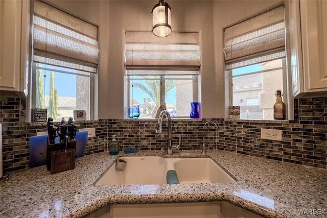 kitchen featuring decorative light fixtures, light stone counters, tasteful backsplash, and a sink