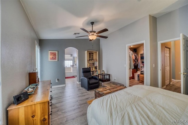 bedroom featuring wood finished floors, visible vents, lofted ceiling, arched walkways, and a spacious closet