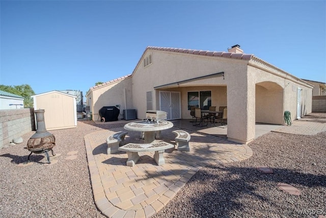 rear view of house featuring stucco siding, a patio, a shed, an outdoor structure, and outdoor dining area