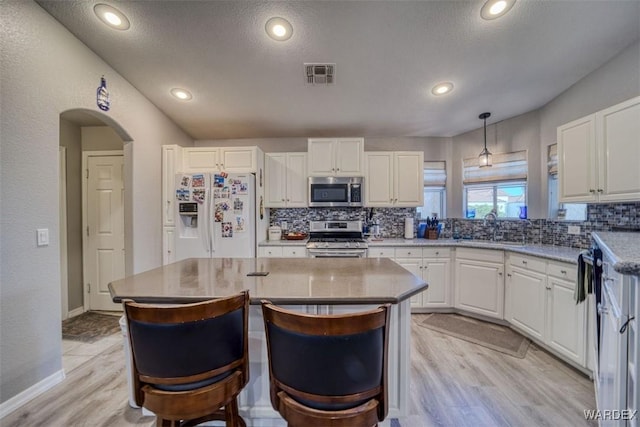 kitchen featuring visible vents, a sink, white cabinetry, arched walkways, and appliances with stainless steel finishes