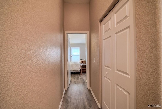 corridor featuring baseboards, wood finished floors, and a textured wall