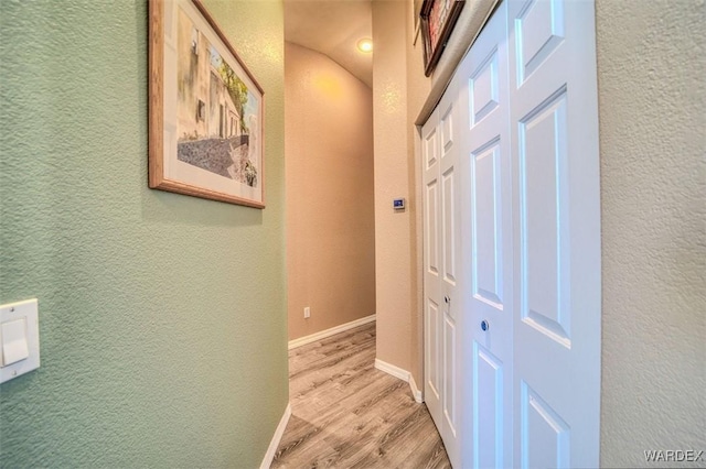 corridor with baseboards, light wood-style floors, and a textured wall