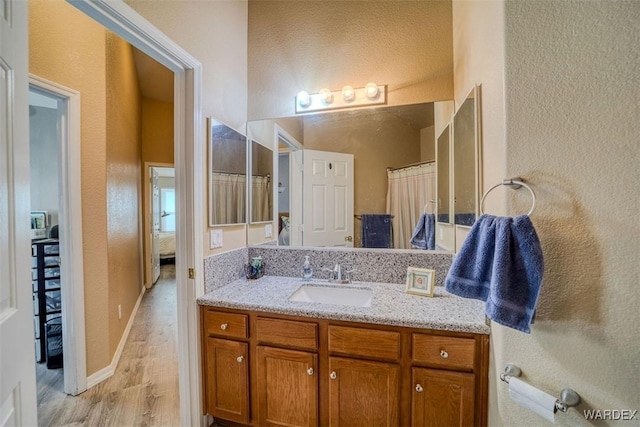 bathroom with ensuite bath, wood finished floors, vanity, and a textured wall