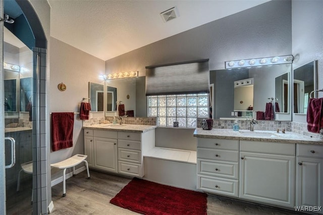 full bath with lofted ceiling, wood finished floors, a stall shower, and a sink