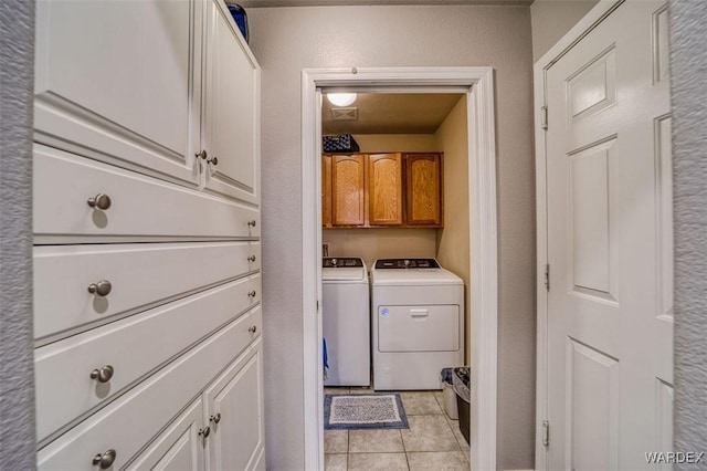 washroom featuring light tile patterned floors, cabinet space, a textured wall, and washing machine and clothes dryer