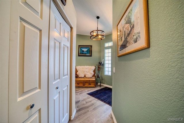 interior space featuring light wood-style flooring, a notable chandelier, a textured wall, and baseboards