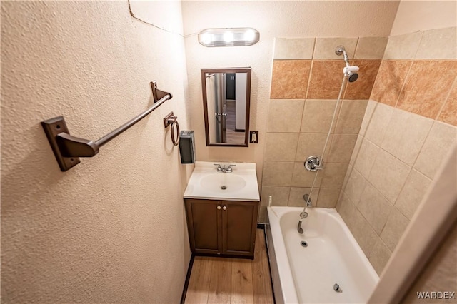 full bathroom with  shower combination, a textured wall, vanity, and wood finished floors