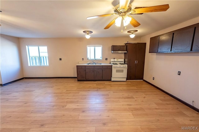 kitchen with white gas stove, dark brown cabinetry, light wood-style floors, light countertops, and a wealth of natural light