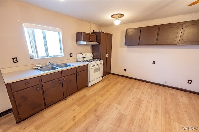 kitchen featuring white gas stove, light countertops, light wood-style floors, a sink, and under cabinet range hood