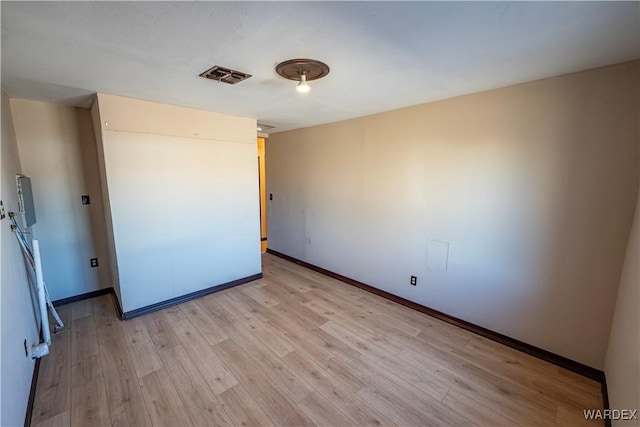 empty room featuring light wood finished floors, visible vents, and baseboards