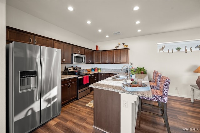 kitchen featuring visible vents, appliances with stainless steel finishes, dark wood-style flooring, a kitchen bar, and a sink