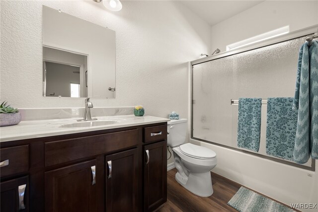 bathroom featuring a textured wall, toilet, shower / bath combination with glass door, wood finished floors, and vanity