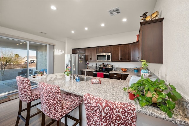 kitchen with stainless steel appliances, recessed lighting, visible vents, light wood-type flooring, and a kitchen breakfast bar