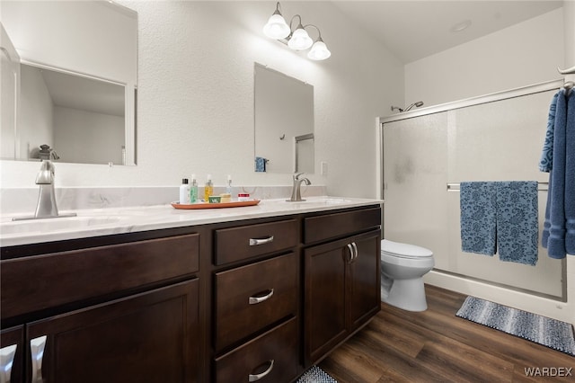 bathroom with double vanity, a shower stall, a sink, and wood finished floors