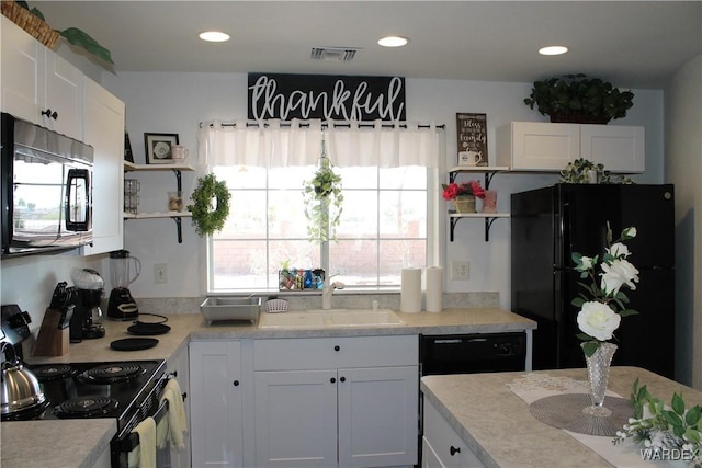 kitchen featuring visible vents, light countertops, black appliances, white cabinetry, and a sink