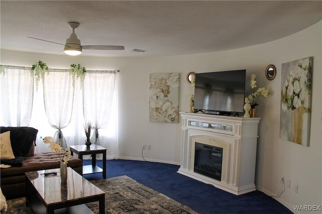 living area featuring visible vents, a ceiling fan, baseboards, dark colored carpet, and a glass covered fireplace