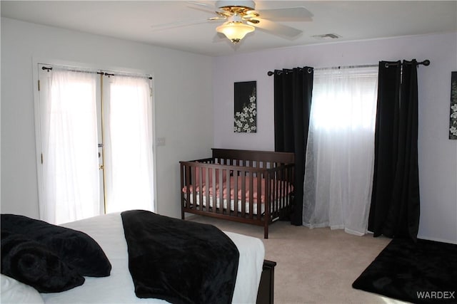 bedroom with a ceiling fan, visible vents, multiple windows, and light carpet