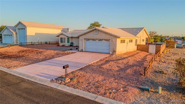 ranch-style house featuring an attached garage, fence, a tile roof, driveway, and stucco siding