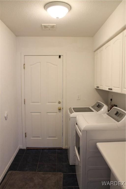 washroom featuring cabinet space, visible vents, washer and clothes dryer, baseboards, and dark tile patterned floors